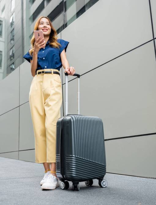 Tourist on vacation waiting at the airport with suitcase and using mobile phone app to check for directions. Asian woman traveler using smartphone app in airport terminal is the focus.
